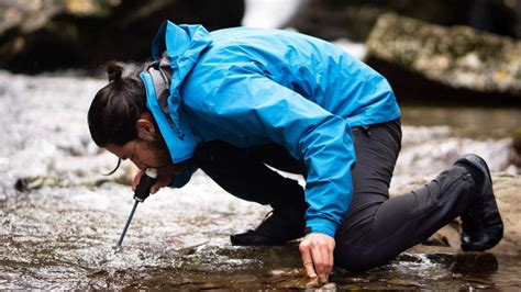 Persona bebiendo agua de un río con un filtro portátil